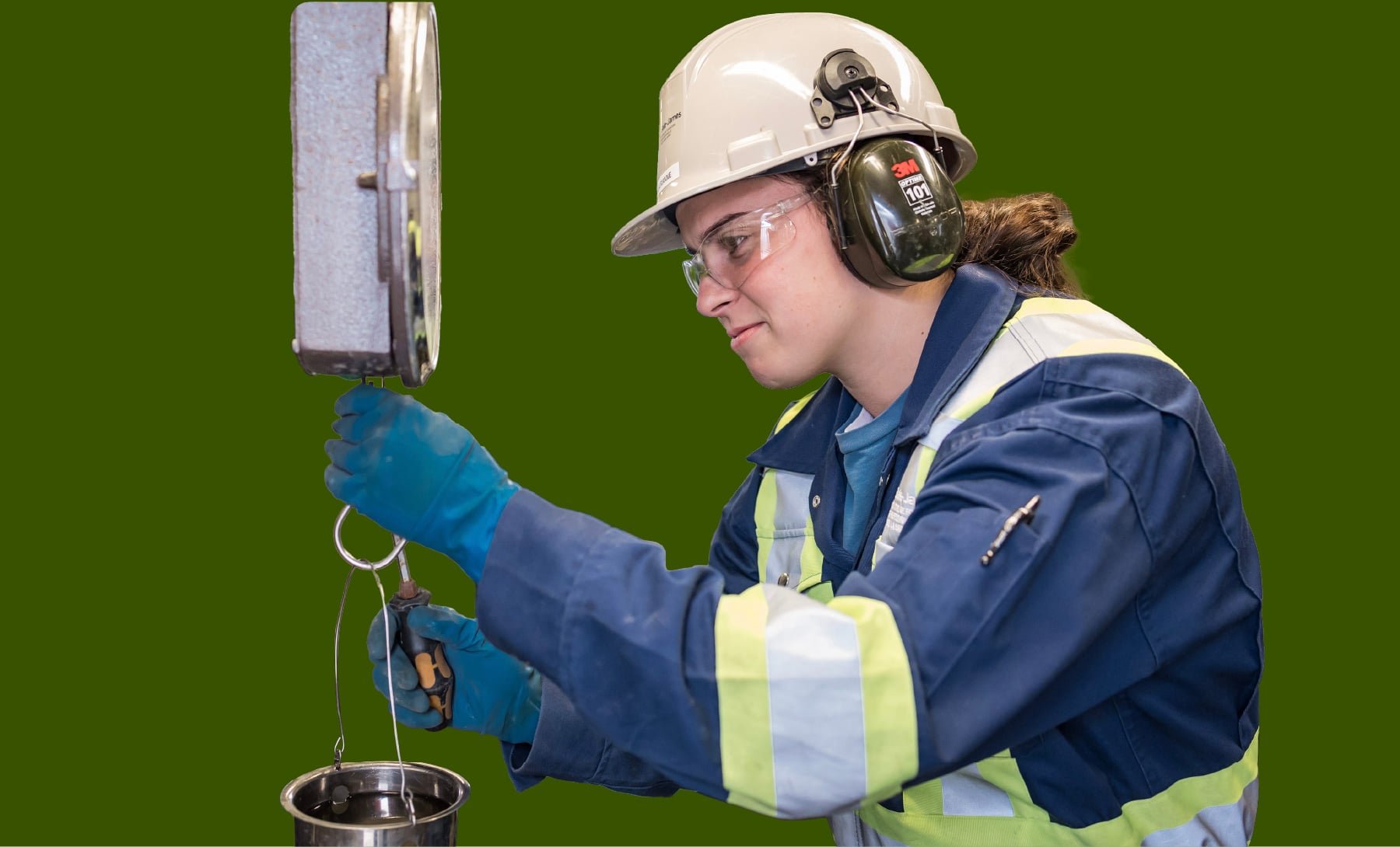 Une femme portant un casque de sécurité pèse un échantillon à l’aide d’une balance suspendue.